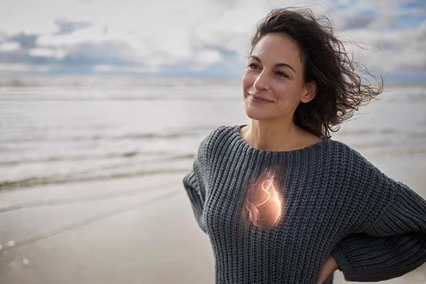 A woman stands on a windy beach, her hair blowing in the wind. There's a heart overlayed on to her chest to provide an example of her vital organ.